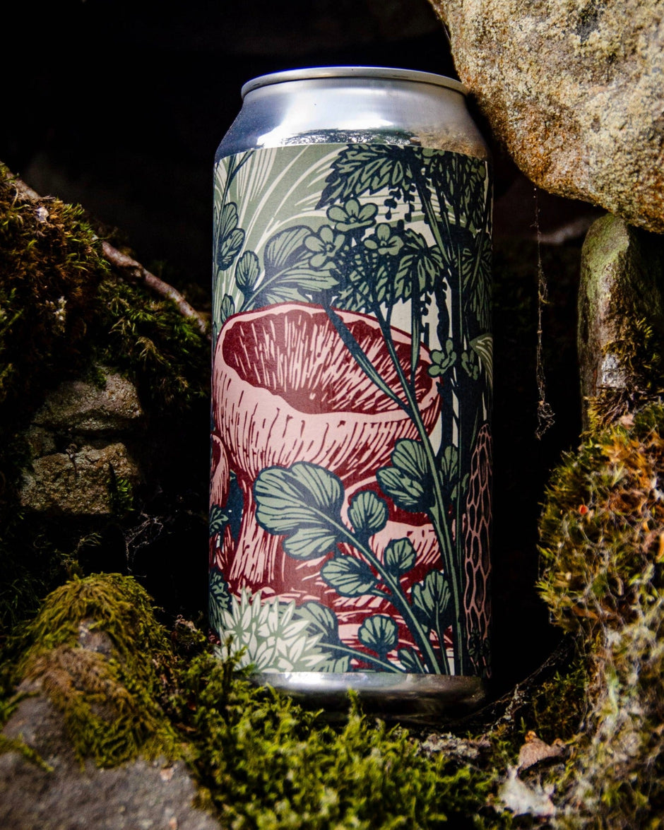 A slim aluminum craft beer can with a detailed botanical mushroom illustration, set in a natural mossy rock environment.